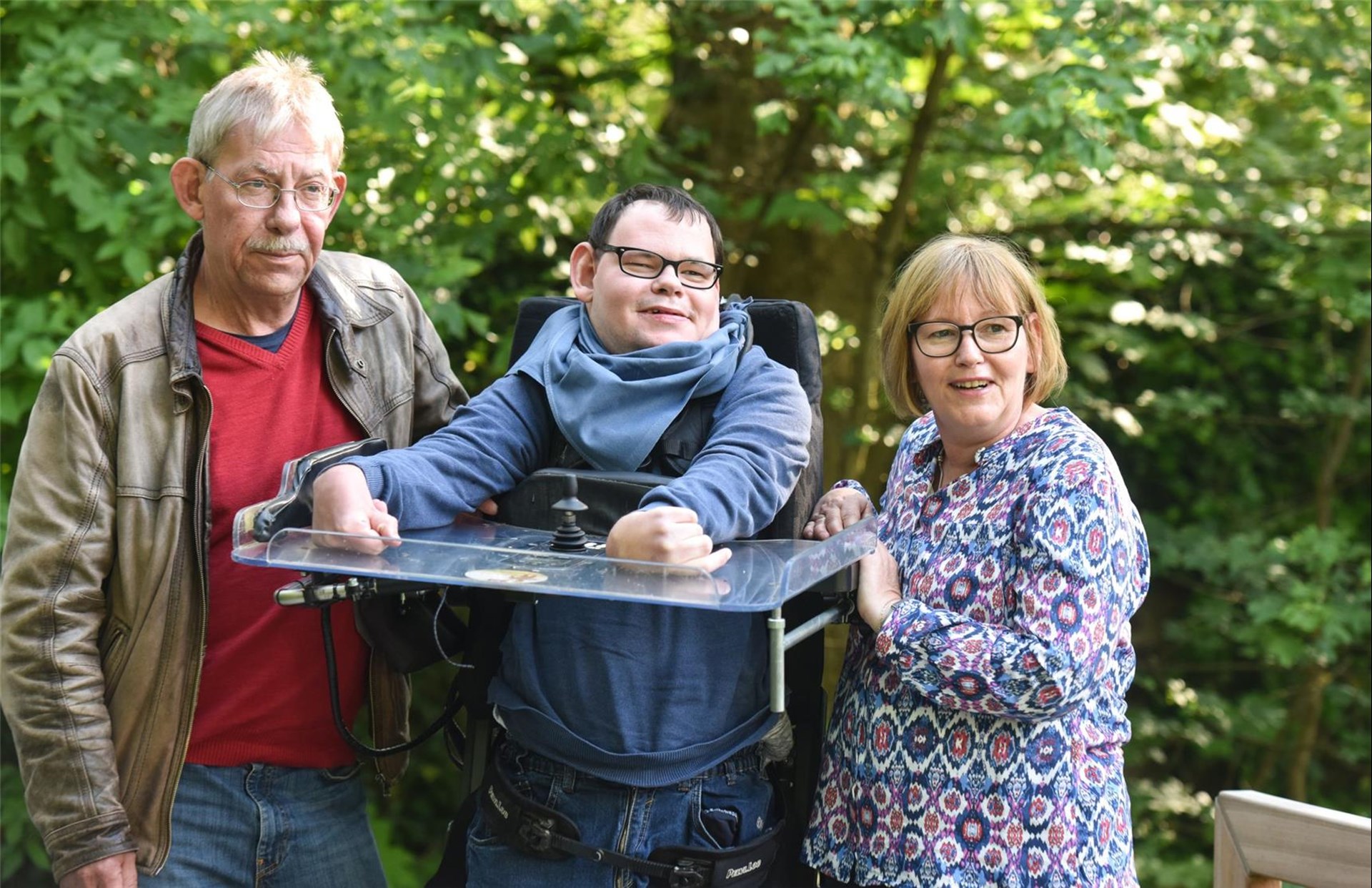 Eltern stehen mit ihrem Sohn mit Behinderung im Grünen