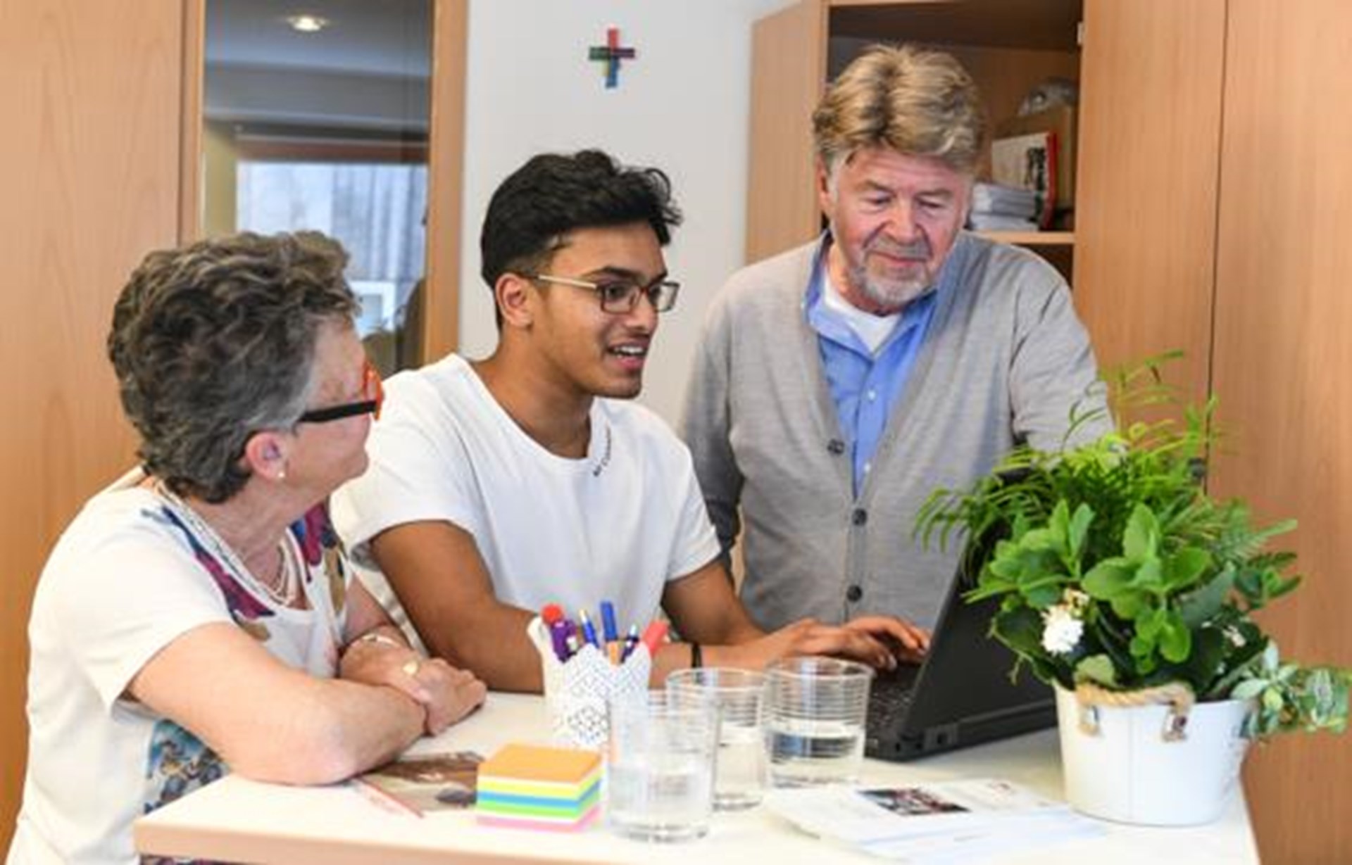 junger Mann mit Migrationshintergrund erklärt älteren Menschen den Umgang mit dem PC